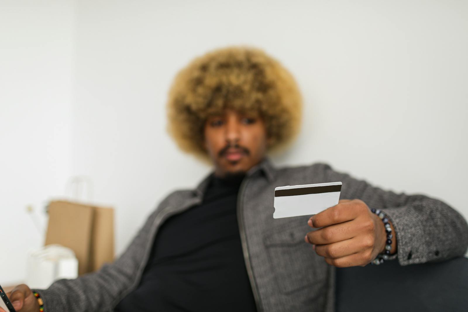 An African American man with afro hair is holding a credit card, making an online purchase indoors.